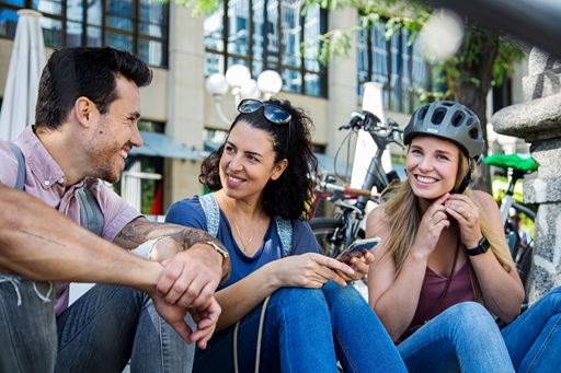Mann und zwei Fragen sitzen auf Bordstein und unterhalten sich mit Fahrrädern im Hintergrund