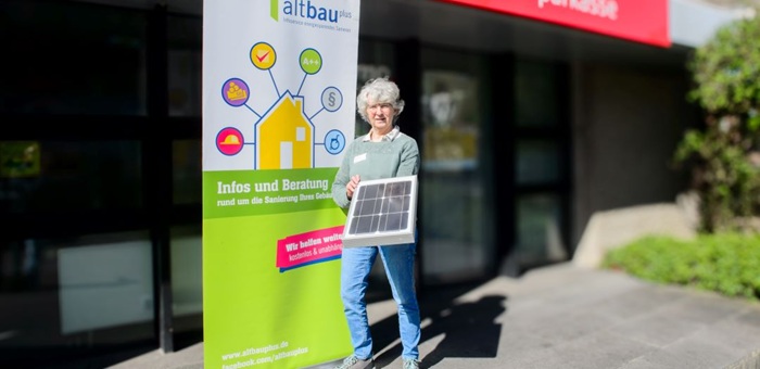 Woman stands in front of a building with a small solar panel in her hand and next to a Roll Up