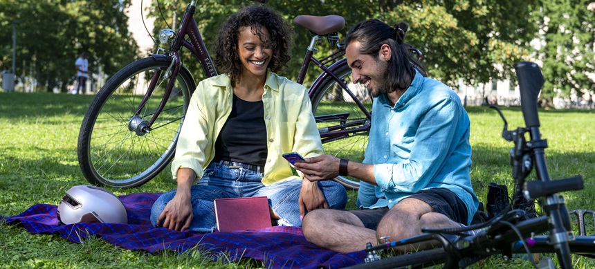 Two people sitting on a blanket in a park with bikes and a phone